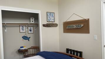 Un dormitorio con cama, cabecera de madera, mesita de noche, una silla, perchero y una pared con letrero que dice 'Fresh Crab'.