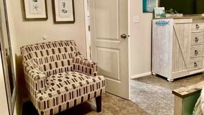 A room with a patterned armchair, a television on a wooden cabinet, and framed pictures on the wall. - 🛟🎣😎Harbor Lite 2BdrmDreamHouse +Loft! AT the PORT. Peeks of Harbor,River,Ocean! (Brookings)