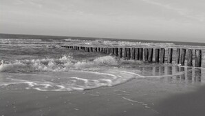 A wooden pier extending into the ocean with waves crashing against it. - Holiday Home in Renesse near Seabeach (Renesse)
