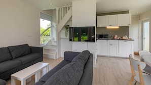 A modern living room with a grey sofa, a white coffee table, and a TV mounted on the wall. - Holiday Home in Renesse near Seabeach (Renesse)