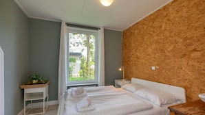 A bedroom with a large bed, a bedside table with a lamp, a small plant, and a window with curtains. - Holiday Home in Renesse near Seabeach (Renesse)