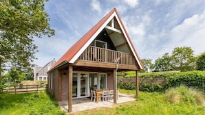 A modern house with a sloped roof, a balcony, and a patio area with a table and chairs. - Holiday Home in Renesse near Seabeach (Renesse)