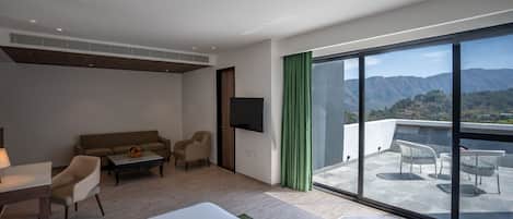 Habitación de hotel moderna con un balcón grande, un sofá, una mesa de comedor y un televisor.