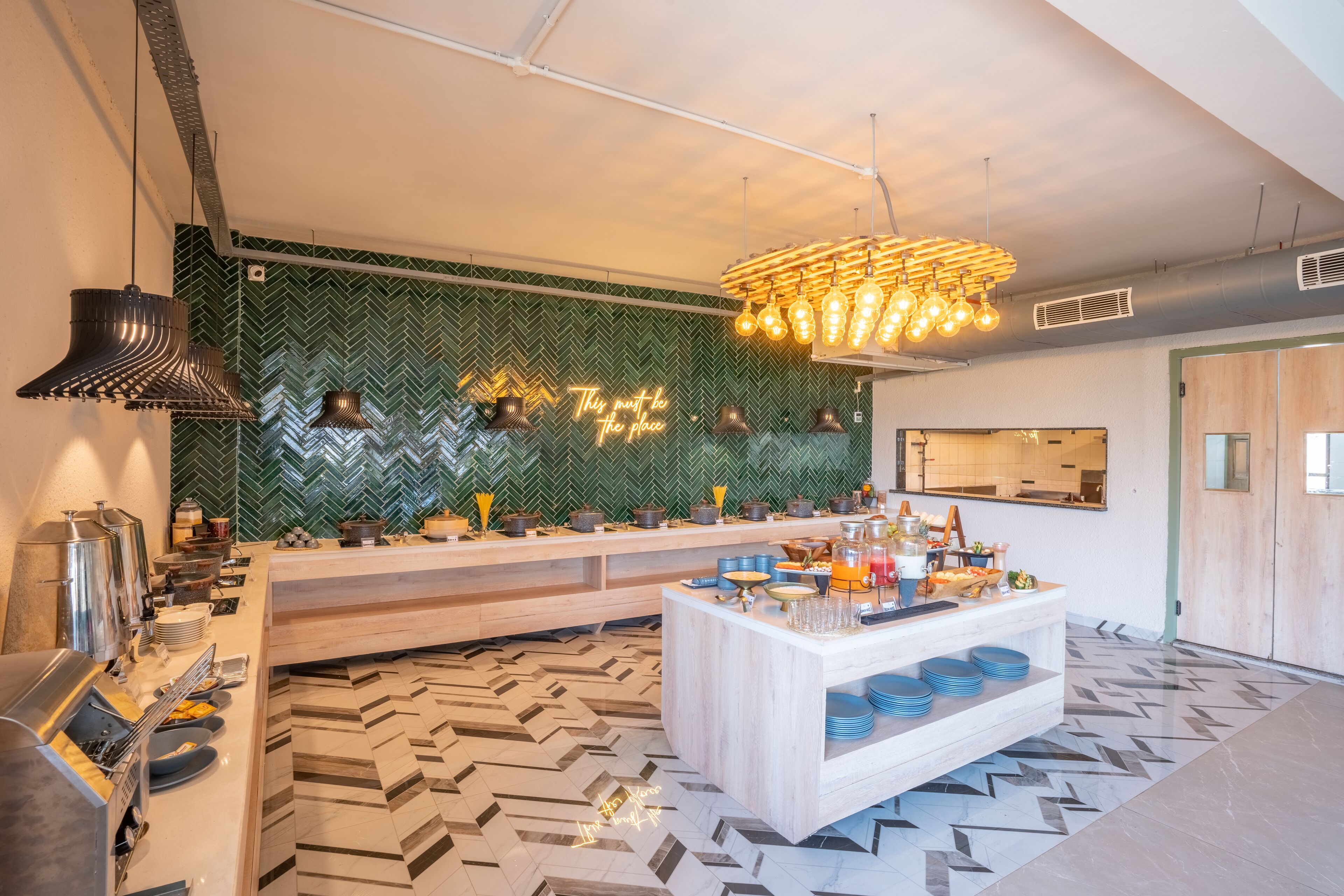 Une cuisine moderne avec un sol à motifs en chevrons, un îlot central orné d’assiettes bleues et un néon mural.