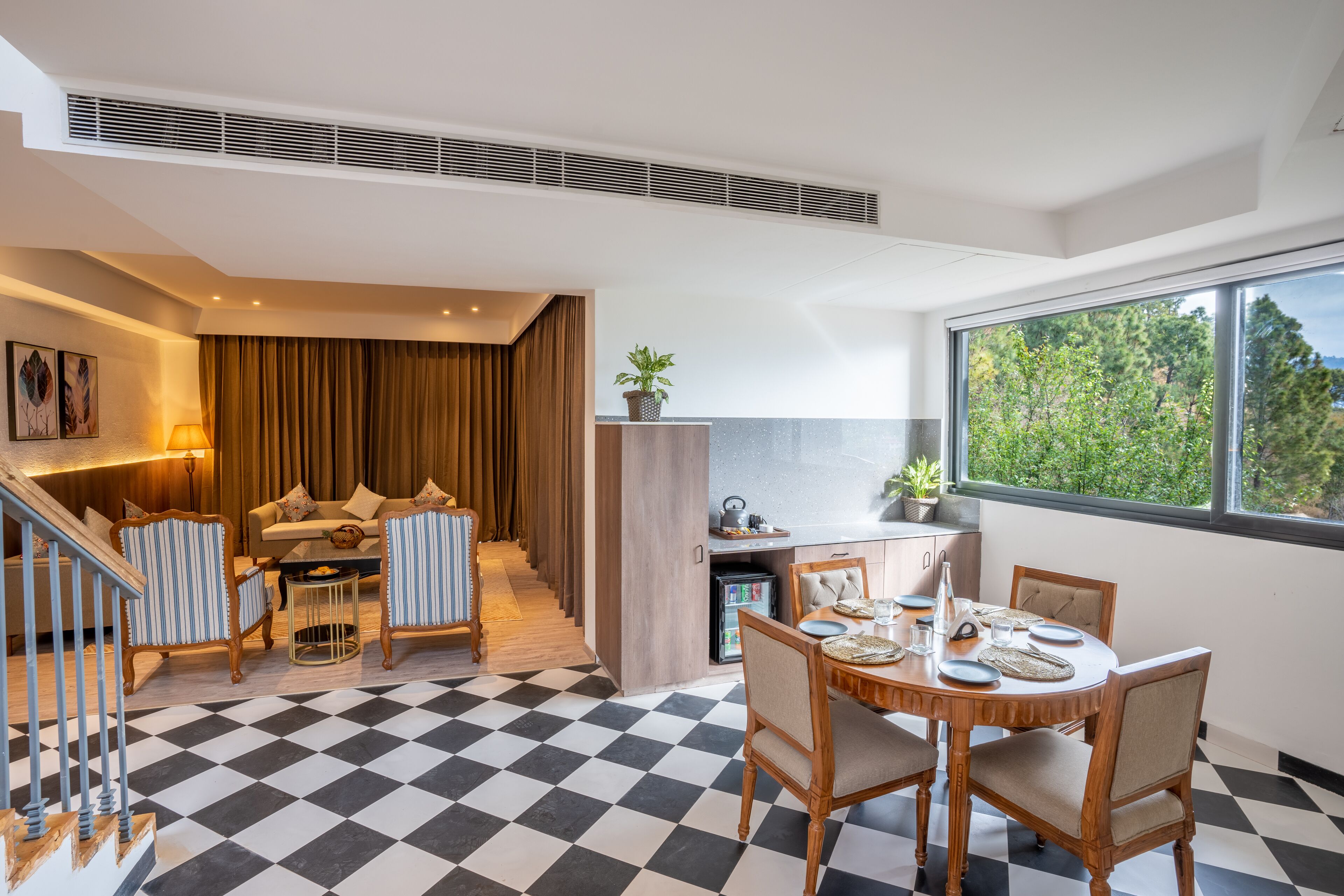 A modern hotel room with a checkered floor, a dining area with a table set for four, a sofa set, and a staircase leading to another level.