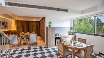A modern hotel room with a checkered floor, a dining area with a table set for four, a sofa set, and a staircase leading to another level.