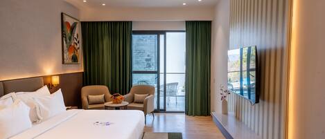 Habitación de hotel con una cama grande, un escritorio, una silla, un televisor y un balcón con cortinas.