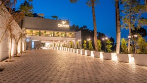 Un edificio moderno con un letrero que dice "VELMORE Royal Grove Athletes". Cuenta con un área de entrada pavimentada, macetas y árboles altos.