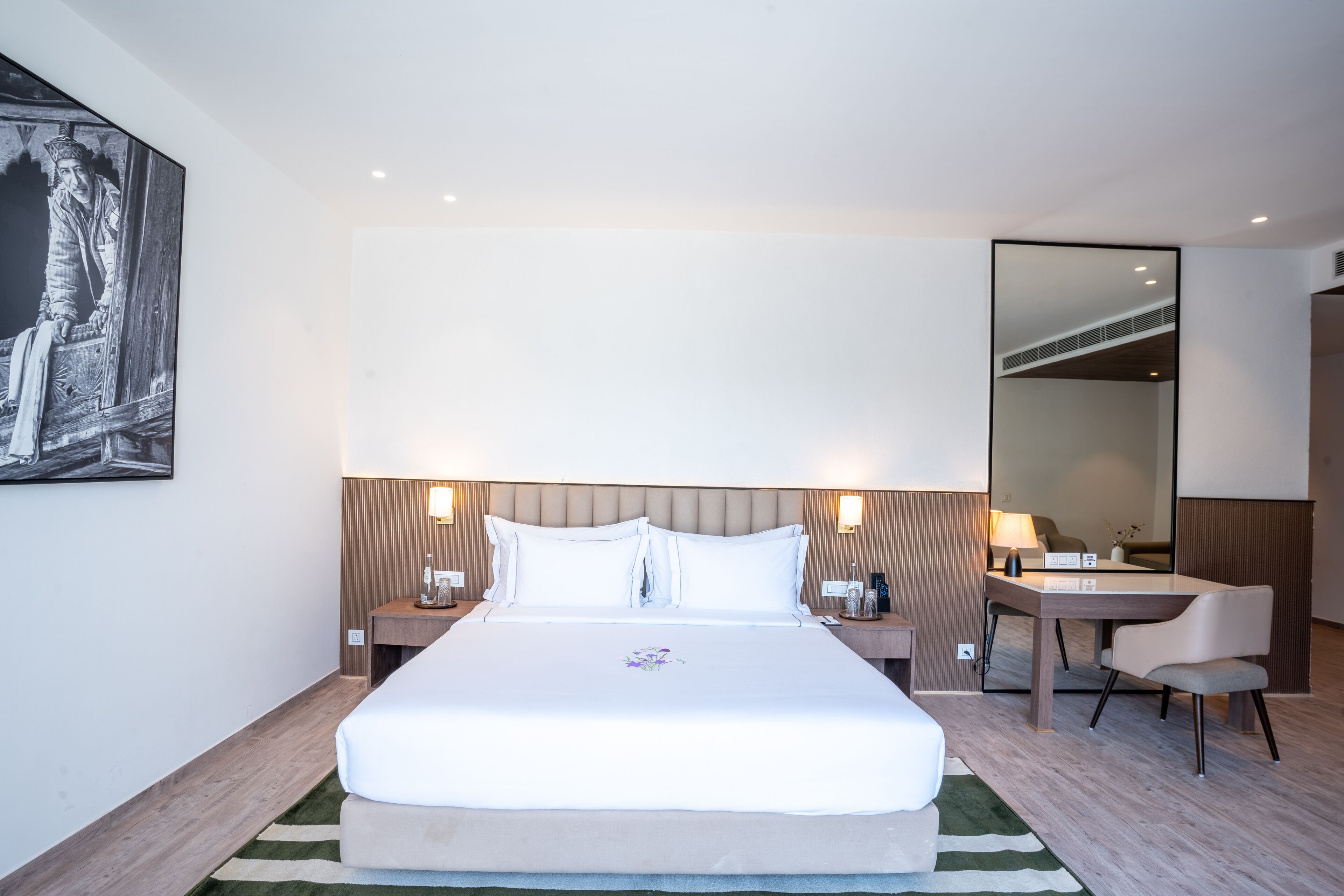 A hotel room with a large bed, a desk, a chair, a mirror, and a nightstand.