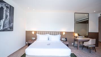 Una habitación de hotel con una cama grande, un escritorio, una silla, un espejo y una mesita de noche.