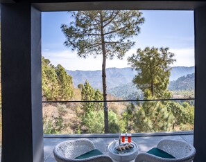 Un balcón con sillas de mimbre, una mesa con bebidas y vistas a la montaña.