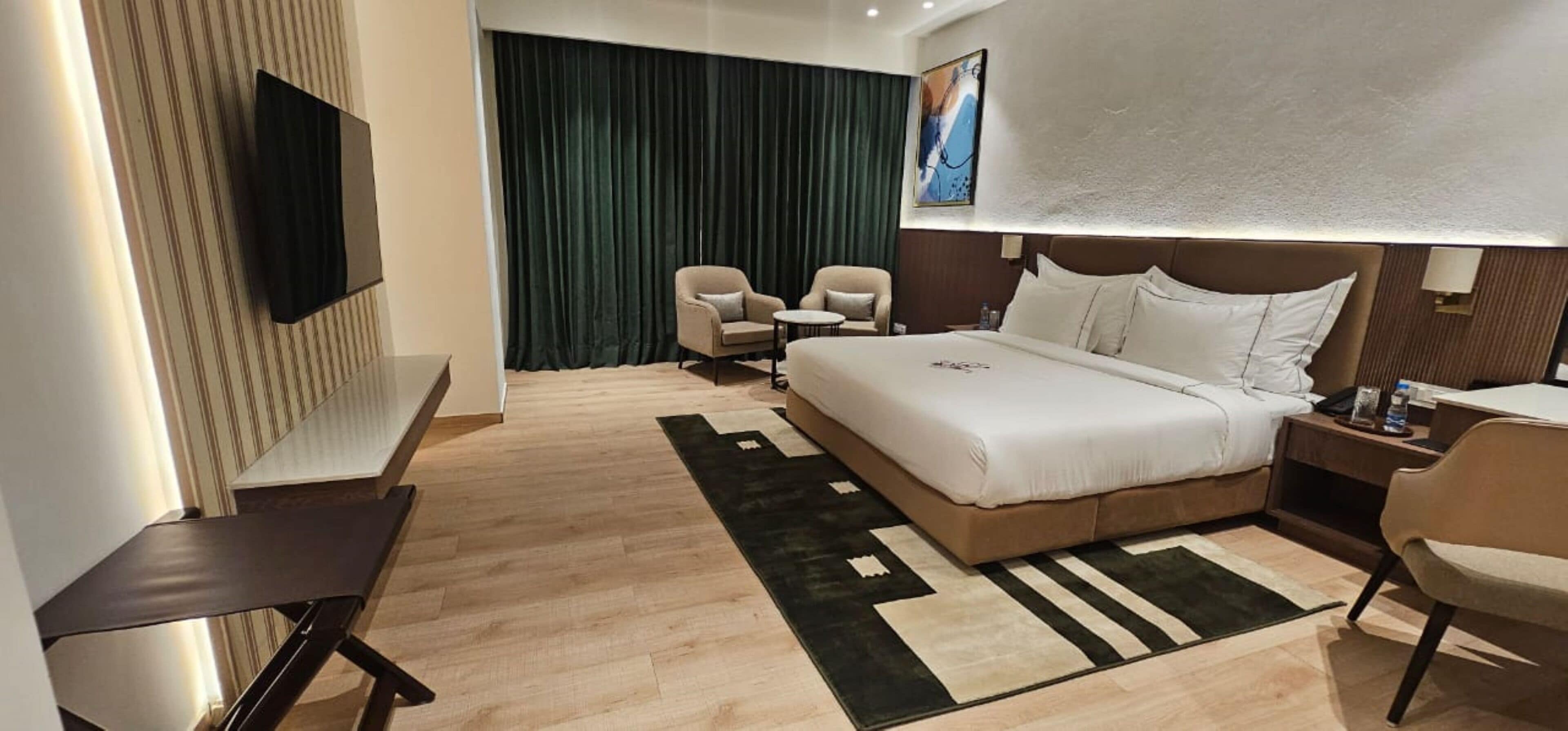 Ein Hotelzimmer mit einem großen Bett, einem Schreibtisch, einem Stuhl, einem Fernseher und Blick nach draußen.