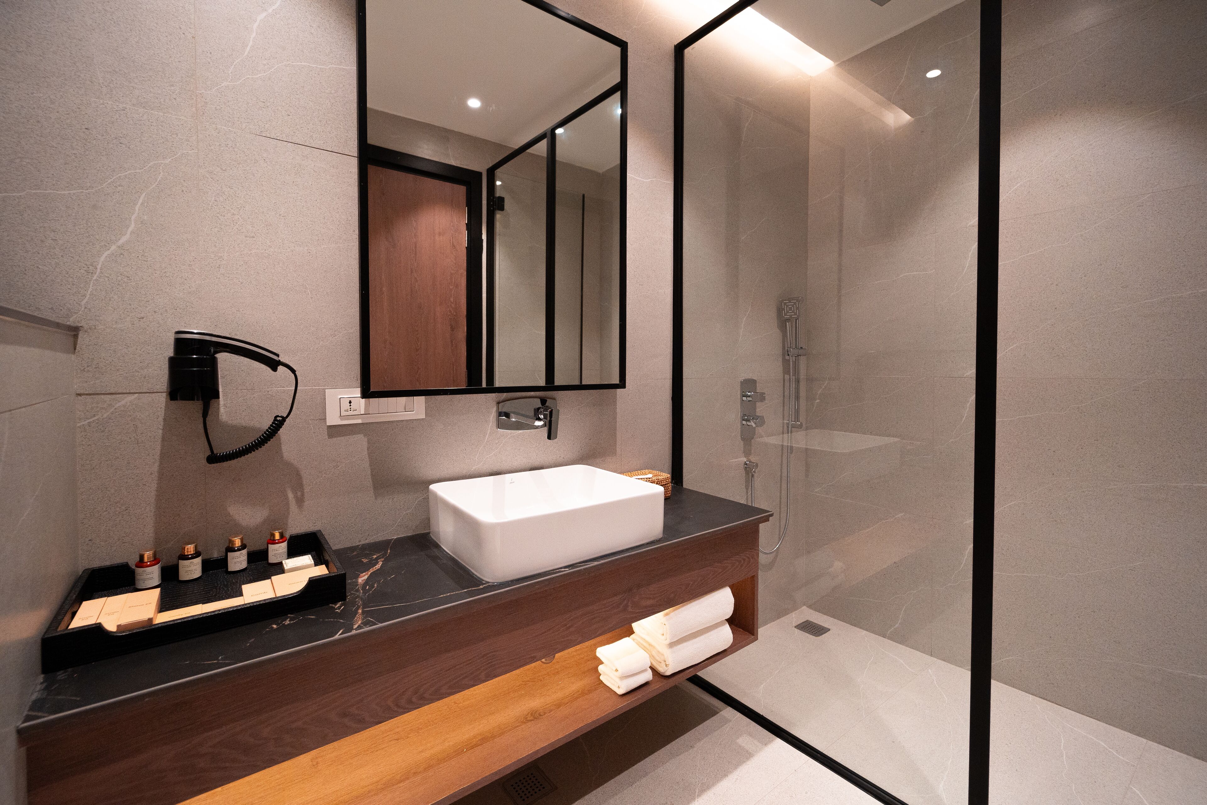 A modern bathroom with a large mirror, a white sink, and a wooden vanity.