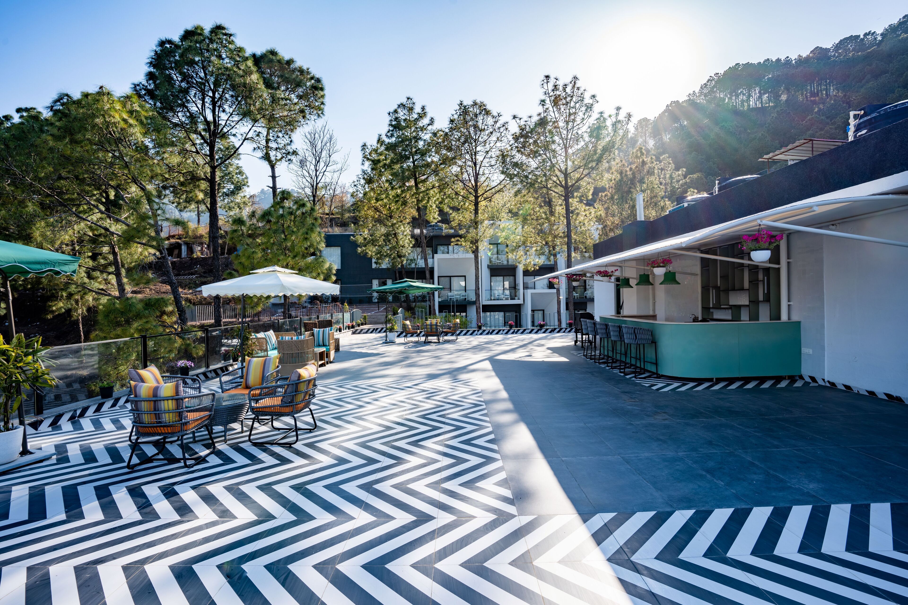 An outdoor patio with a black and white chevron-patterned floor, seating area with chairs and tables, and a bar area with hanging plants.