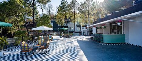 An outdoor patio with a black and white chevron-patterned floor, seating area with chairs and tables, and a bar area with hanging plants.