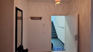 Un pasillo con piso de madera, una lámpara colgante, un espejo y una escalera que conduce a otra habitación.
