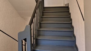 Eine Treppe mit dunklen Stufen und schwarzen Spindeln, die zu einer Zwischenebene mit einer weißen Wand und einem kleinen Fenster führt.