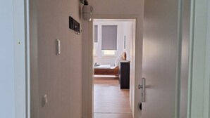 Ein Flur, der zu einem Schlafzimmer mit Bett, Schminktisch und einem Fenster mit Jalousien führt.