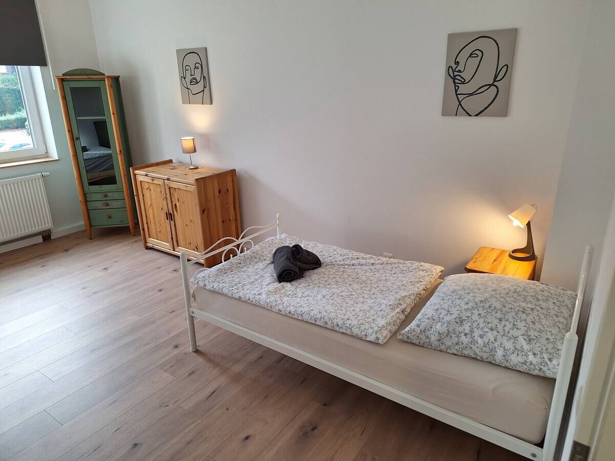A single bed with a wooden headboard, a nightstand with a lamp, and a wardrobe with a mirror.