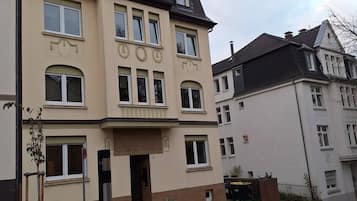 Ein mehrgeschossiges Wohngebäude mit symmetrischer Fassade, großen Fenstern und einem zentralen Eingang.