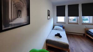 Une petite pièce bien éclairée, avec un lit, un fauteuil vert et un tableau encadré accroché au mur.