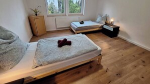 A small, well-lit bedroom with a single bed, a nightstand, a radiator, and a window with blinds.