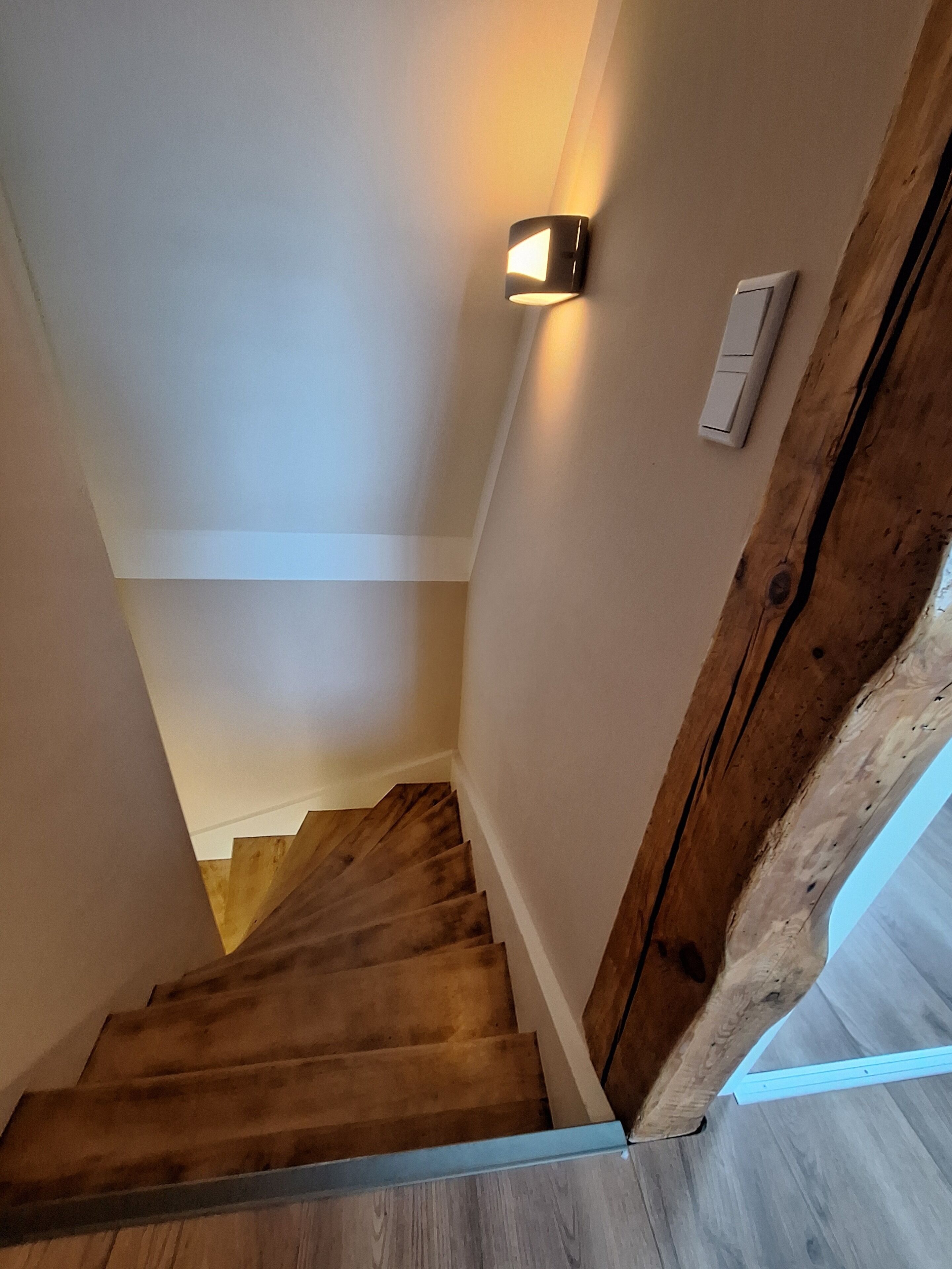Un escalier en bois avec un luminaire fixé au mur.