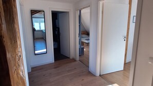 Ein geräumiges Zimmer mit Holzboden, weißen Wänden und einer schrägen Decke. Mehrere Türen führen in andere Räume.