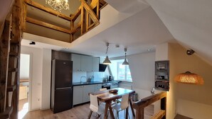 Eine moderne Küche mit integriertem Kühlschrank, ein Essbereich mit Holztisch und Stühlen sowie eine Treppe, die zu einer oberen Ebene mit einer Pendelleuchte führt.