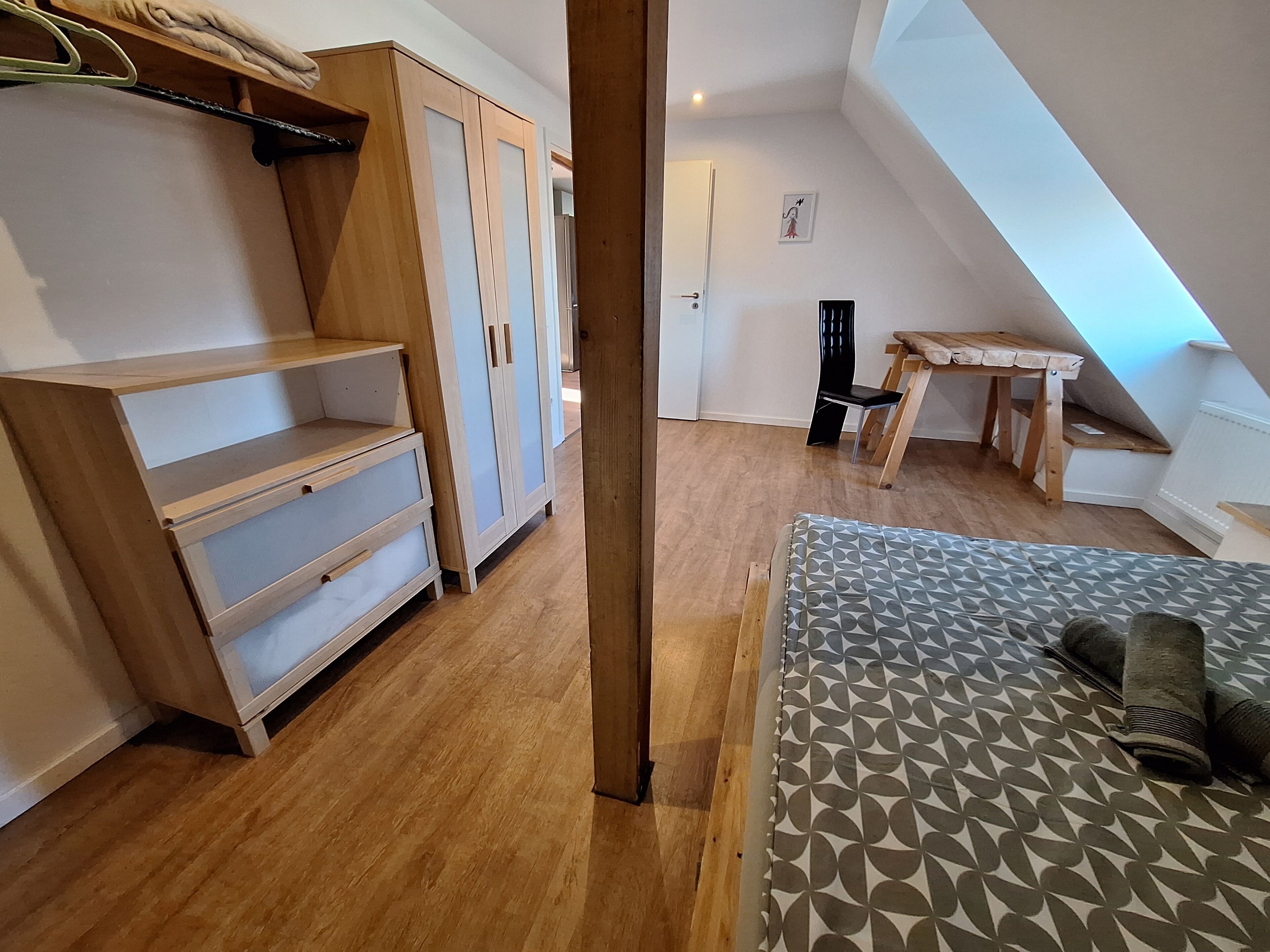 A bedroom with a bed, wooden wardrobe, and a small desk.