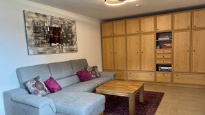 Een woonkamer met een grijze bank, een houten salontafel en een rood tapijt met een patroon.