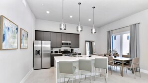 Une cuisine moderne dotée d’appareils électroménagers en acier inoxydable, d’un îlot central avec des tabourets, d’un éclairage suspendu et d’un coin repas comprenant une table et des chaises.