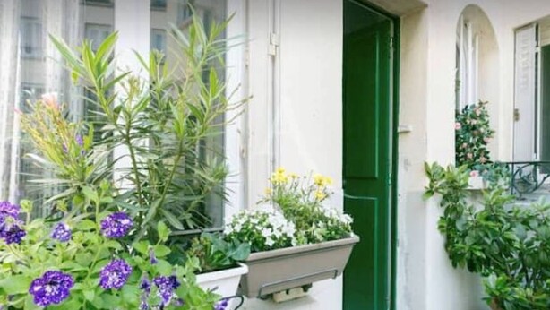 A building with a green door and windows, surrounded by potted plants and flowers. - Apartment Studio in Small renovated house in Paris (Paris)
