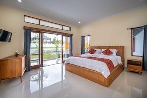A spacious bedroom with a large bed, a wooden nightstand, a TV, and a sliding glass door leading to a balcony. - The Patra Ubud (Ubud)