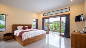 Um quarto espaçoso com uma cama grande, uma mesinha de cabeceira de madeira, uma TV de tela plana e uma porta de vidro corrediça para uma varanda.