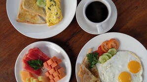 Mesa de café da manhã com torradas, omelete, café e um prato com tomates, pepinos e salada.