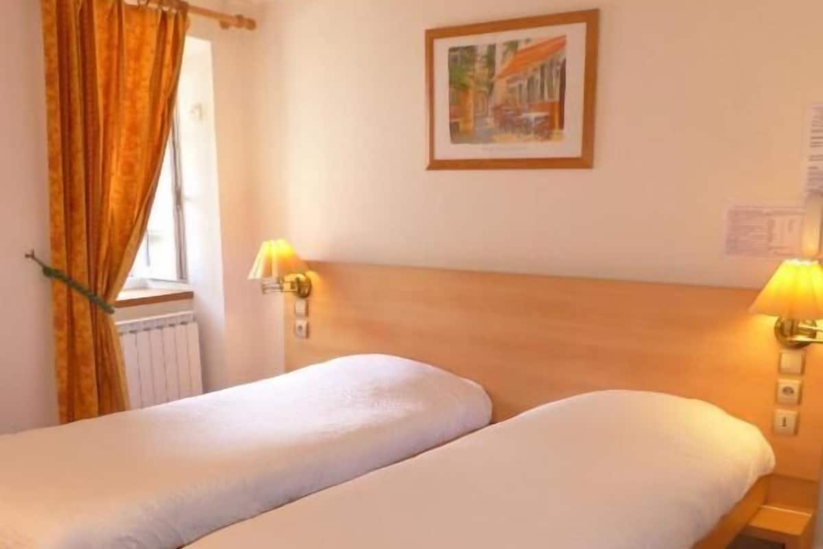 A hotel room with two single beds, a wooden headboard, a window with curtains, and two wall-mounted lamps.