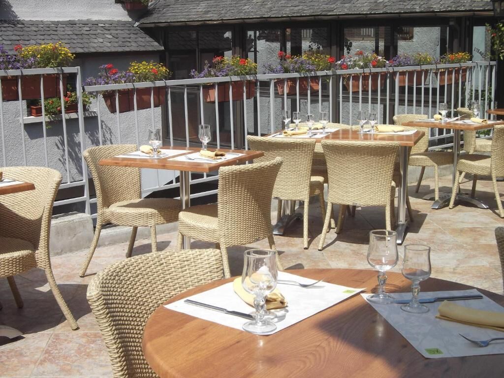 Un espace de restauration en plein air avec des chaises en osier et des tables en bois, dont certaines sont équipées de verres à vin et de menus.