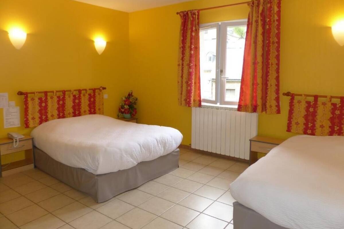 A hotel room with two beds, yellow walls, and a window with red curtains.