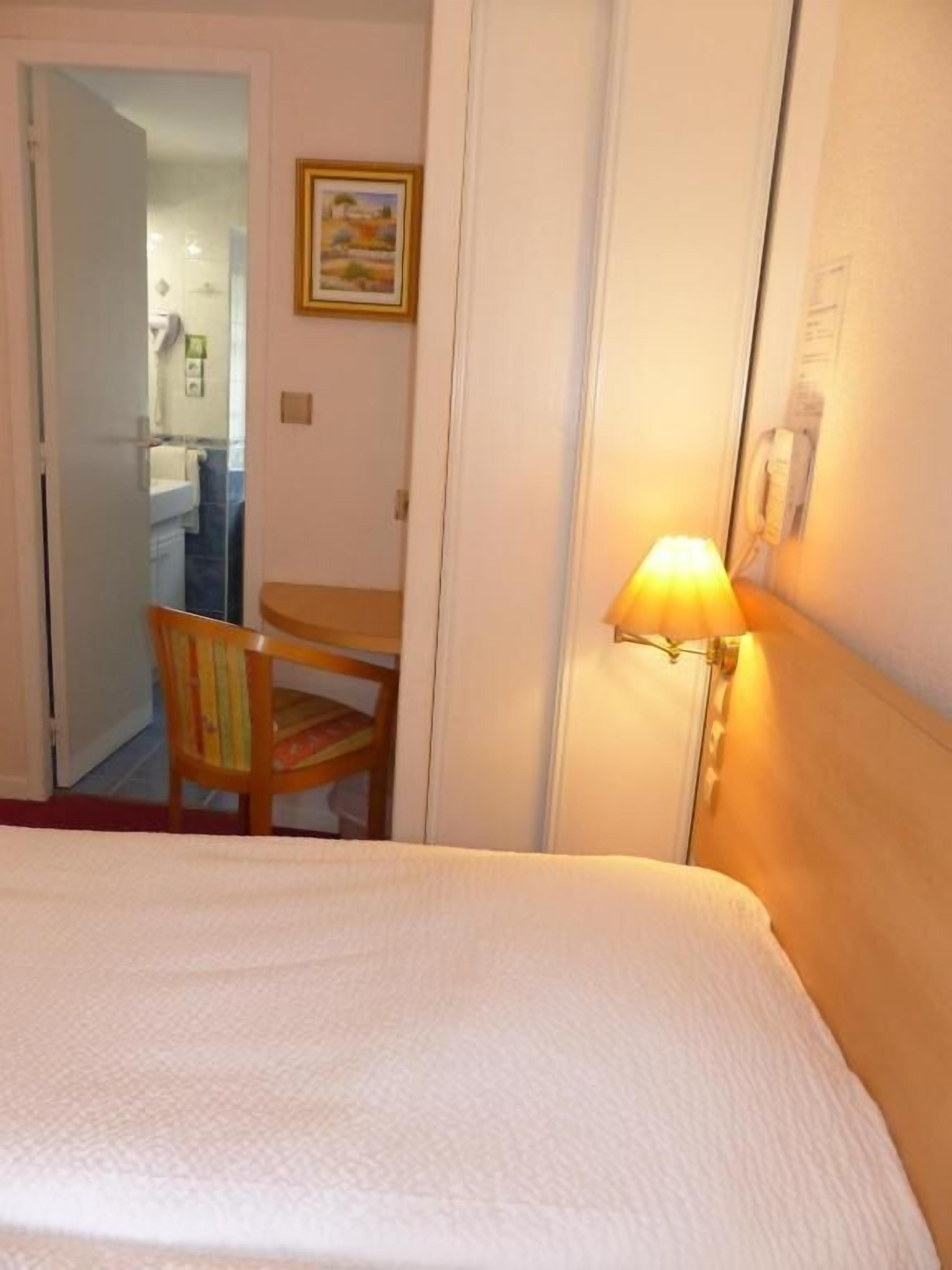 A hotel room with a bed, a desk, a chair, and a lamp.