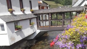 A riverside building with a stone foundation, a wooden bridge, and a variety of colorful flowers along the water's edge. - Hotel Auberge de l'Isard (Saint-Lary)