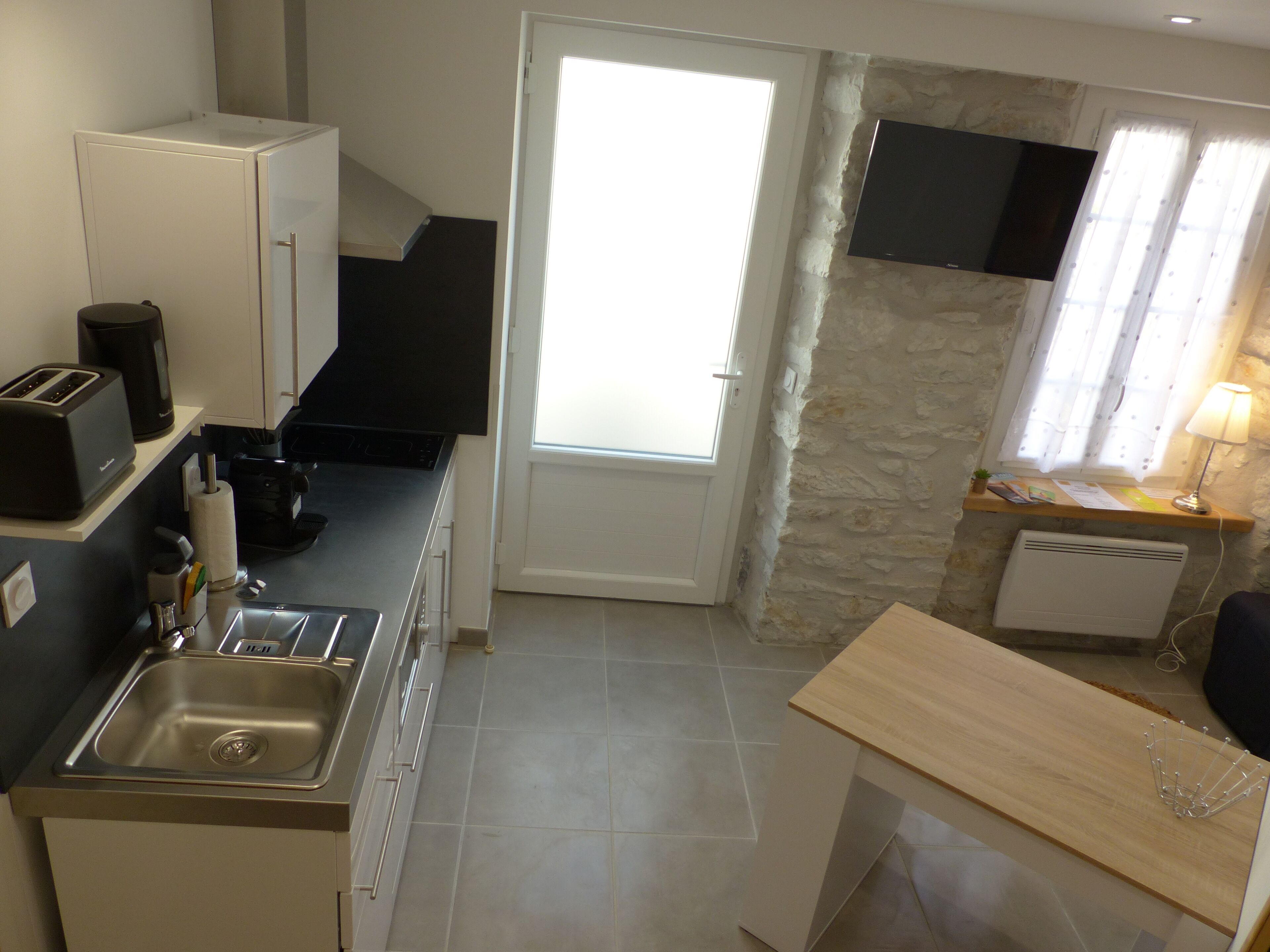 Una cocina compacta con lavamanos, tostadora, cafetera y una ventana pequeña con cortinas.