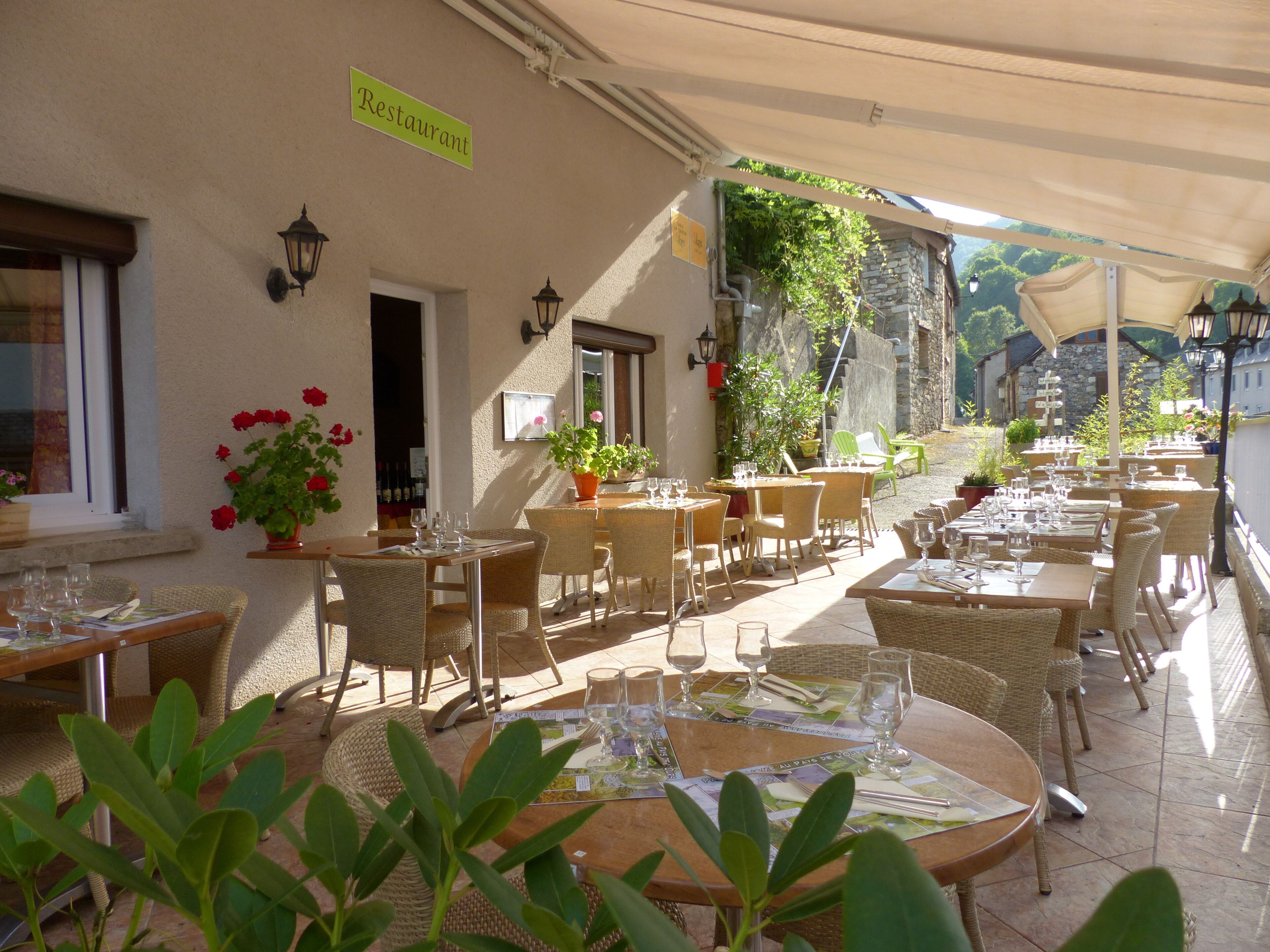 Un restaurant en plein air avec des tables et des chaises en osier, des plantes en pot et un panneau indiquant qu’il s’agit d’un restaurant.
