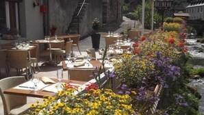 An outdoor dining area with tables and chairs, surrounded by potted flowers and a view of a river. - Hotel Auberge de l'Isard (Saint-Lary)