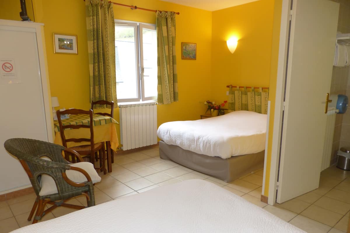 A bedroom with a bed, a chair, a table, a radiator, and a window with curtains.