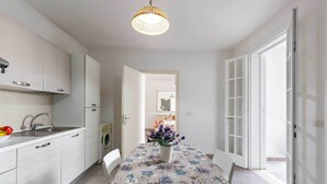 A modern kitchen with white cabinets, a stainless steel sink, and a dining area with a table covered by a floral tablecloth. - 3725 Villino Marisun by Barbarhouse (Porto Cesareo)