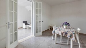 A dining area with a table set for two, a chair, and a small table with a vase of flowers. - 3725 Villino Marisun by Barbarhouse (Porto Cesareo)