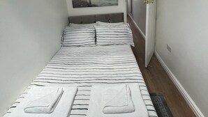Een smalle hotelkamer met een bed, een schilderij van een strand en een deur die naar een andere kamer leidt.