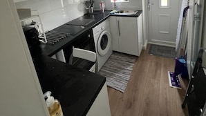 Een compacte keuken met witte kastjes, een zwart aanrecht, een wasmachine en een klein raam.