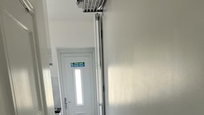 Een gang met een witte deur, een nooduitgangsbord en een radiator aan de muur.